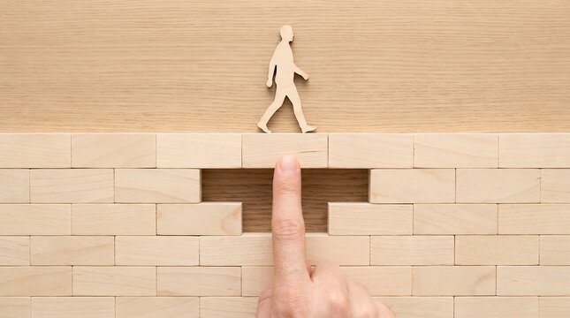 A wooden figure of a person walks across a gap in a wall of wooden blocks with a finger supporting the path progress challenge solution obstacle overcoming concept achievement