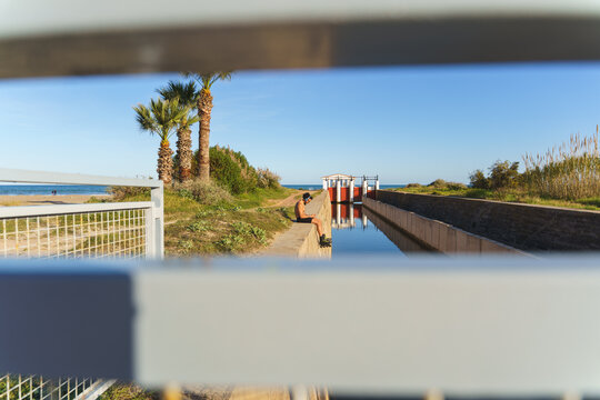Man with rollerblades sitting by a canal with palms and beach in the background