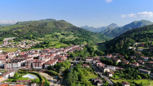 Wide aerial drone video of Cangas de Onis, Spain with its historic medieval Roman bridge over the Sella River and view of the Picos De Europa 