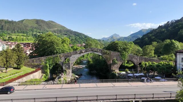 Drone footage historic Roman-medieval Bridge in Cangas de Onis, Spain. Aerial video rising up towards old bridge in Asturias region of northern Spain with the Picos de Europa in the distance.