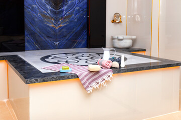 Traditional Turkish bath platform with marble basin and spa accessories. Elegant hammam interior with decorative blue stone wall. Wellness relaxation concept. Close-up.