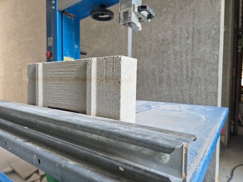 Close-up front view of an industrial band saw with an AAC aerated concrete block on it at a construction site.