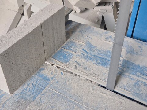 Close-up diagonal view of a band saw blade with an AAC concrete block and cut dust debris in the background.