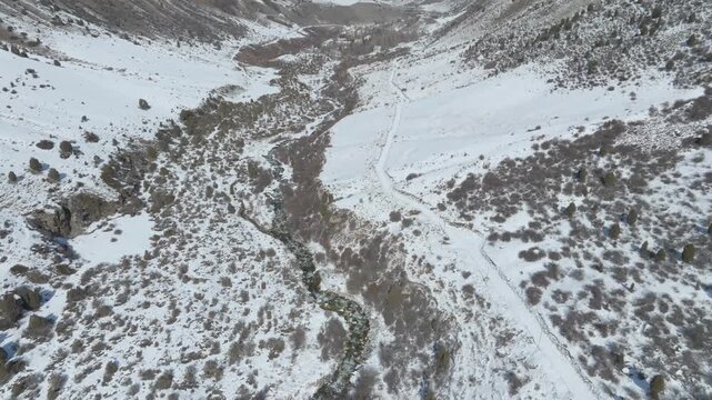 Drone footage flying over the snow-covered Issyk-Ata Gorge valley with a winding river and rugged mountains, Chuy Region, Kyrgyzstan in clear winter daylight