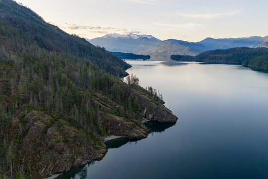 Calm Mountain Lake Panorama With Forested Cliffs And Snowy Peaks Over Harrison Lake, BC, Canada