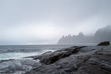 Fototapeta premium The dramatic 'Devil's Teeth' rock formations at Tungeneset viewpoint on the stormy Norwegian coast with misty mountains in the distance.