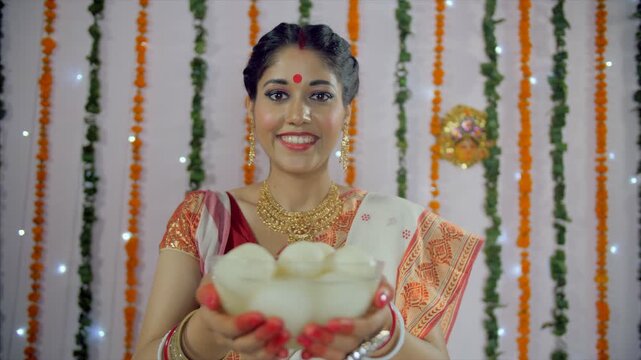 A beautiful Bengali lady offering a bowl full of sweets (Rasgulla) during a festival. An Indian housewife in a Bengali saree giving Roshogolla to her friends to welcome them - Durga Puja Concept