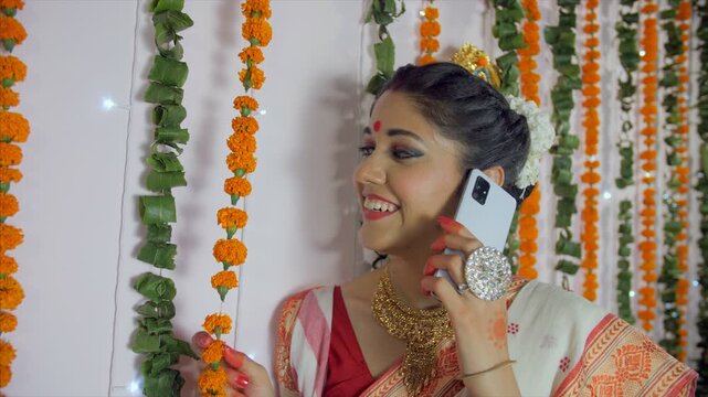 Beautiful Indian female happily greeting her friends over a call on Durgotsava. Medium shot - Traditional Bengali woman in ethnic sari/saree  talking on a phone during Durga Puja celebration