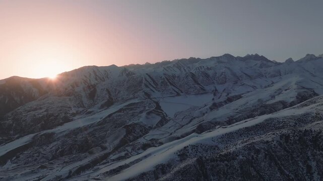 Drone footage of sunrise light over snow-covered ridges and winding roads in Chunkurchak Valley, Chuy Region, Kyrgyzstan, winter mountain landscape with copy space