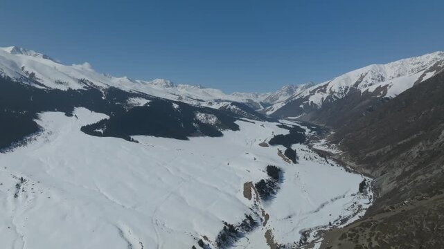 Drone footage of Grigoryev Gorge with wide snow-covered valley, rugged peaks and clear blue sky in Issyk-Kul Region, Kyrgyzstan, scenic winter travel landscape