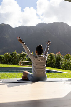 Yoga mat resting on wooden deck beside rectangular pool, facing mountain range under clouds