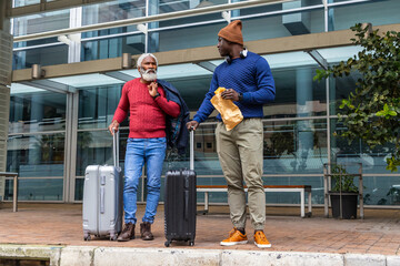 Standing two men with suitcases wearing red and blue sweaters on plaza, with paper bag, headphones © wavebreak3
