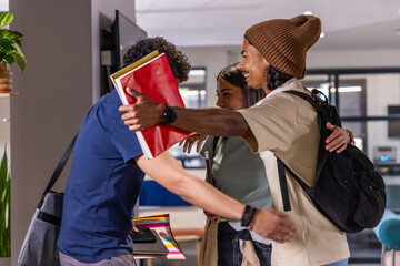 Teenage students hugging near table in campus lounge, holding red folder, notebooks, backpacks © wavebreak3