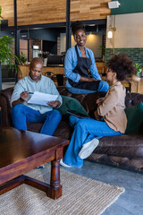 Obraz premium African coworkers reviewing papers with pen, tablet in cafe lounge with apron-clad colleague