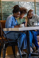 African American friends leaning in at cafe, smiling and viewing smartphone with travel mug, cup © wavebreak3