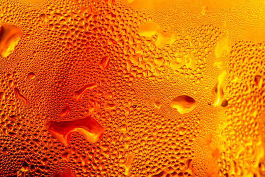 Macro image showing condensation on a cold glass surface, the surface of a drop of cola drink,showcases the intricate texture of water droplets forming condensation on a chilled glass surface,