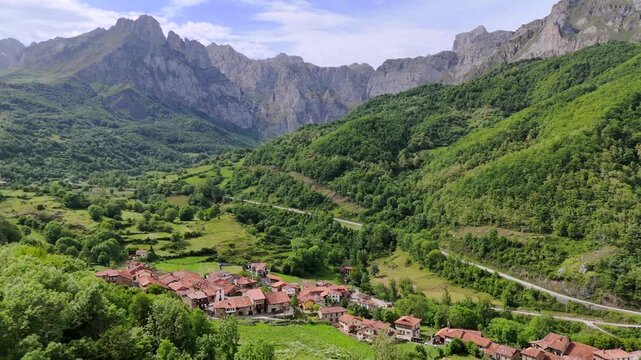 Drone shot moving forward above a rustic alpine village in Cantabria, Spain near Fuente De. Scenic aerial view of mountain landscape with the majestic Picos de Europa Central Massif in background.