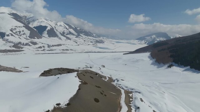 Drone footage of Grigoryev Gorge with snow-covered valley, winding road and mountain ridges under blue sky, Issyk-Kul Region, Kyrgyzstan