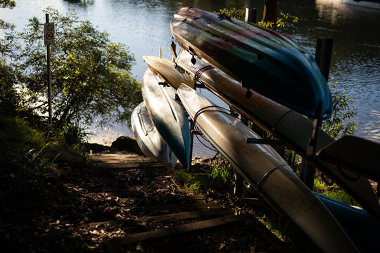 Stacked kayaks near tranquil riverside pathway