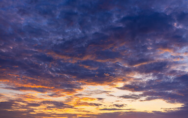Obraz premium Vibrant Golden Hour Sunset Sky with Dramatic Clouds,A stunning view of a colorful sunset sky filled with dramatic, textured clouds glowing in shades of orange, yellow, and deep purple during.