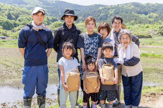 田植え後の水田で収穫物を手に笑顔を見せる三世代家族