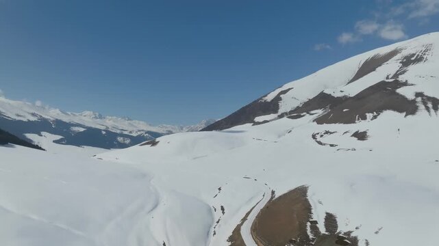 Wide aerial view of snow-covered mountain valley and ridgelines under clear blue sky in Grigoriev Gorge, Issyk-Kul Region, Kyrgyzstan, serene winter nature