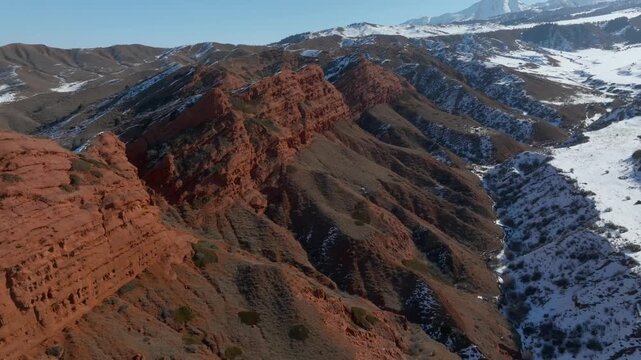 Drone footage of the Jeti Oguz Gorge and the Seven Bulls red sandstone cliffs in Issyk Kul Region, Kyrgyzstan, with winter snow patches on mountain slopes