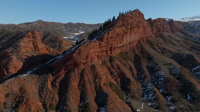 Drone footage of the Seven Bulls red sandstone cliffs and rugged ridges in Jeti Oguz Gorge, Issyk Kul Region, Kyrgyzstan, with patches of snow at sunset light