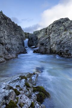 A river flows through a narrow gorge, over a small waterfall, surrounded by steep cliffs, Peer Gynt hytta, Rondane National Park, Otta, Innlandet, Norway