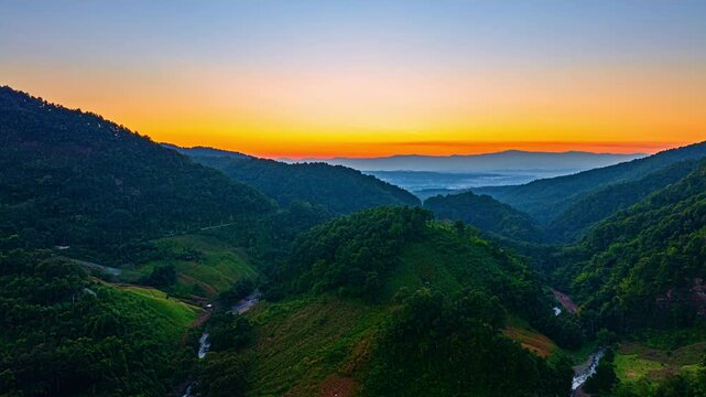 A stunning aerial hyper lapse captures the first light of sunrise spreading across a peaceful mountain valley beneath a colorful sky gradient. Scenic Aerial View of Mountains and Sunrise
