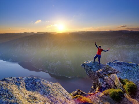 Woman standing with spread arms on a rocky outcrop at Kjerag above the Lysefjord, sunset, Lyseboten, Rogaland, Norway