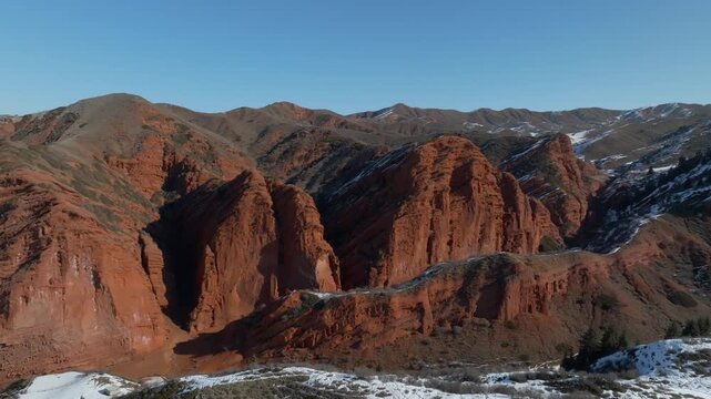 Aerial footage of the Seven Bulls sandstone cliffs and rugged mountains in Jeti-Oguz Gorge, Issyk-Kul Region, Kyrgyzstan on a clear day with snow patches