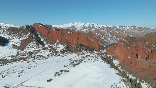 Drone footage of the Jeti Oguz Gorge and Seven Bulls red sandstone cliffs above a snowy valley and mountain ridges near Jeti Oguz, Issyk Kul Region, Kyrgyzstan