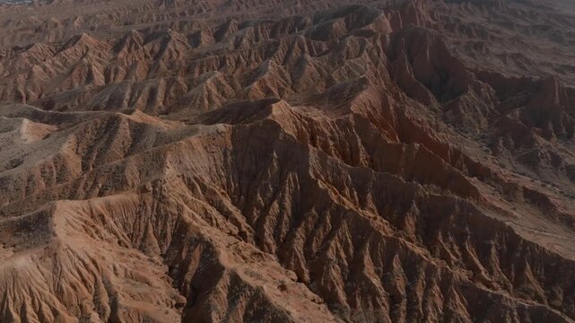 Drone footage over Mars Canyon eroded red sandstone ridges and gullies at golden hour, dramatic desert badlands scenery in Kyrgyzstan, Central Asia