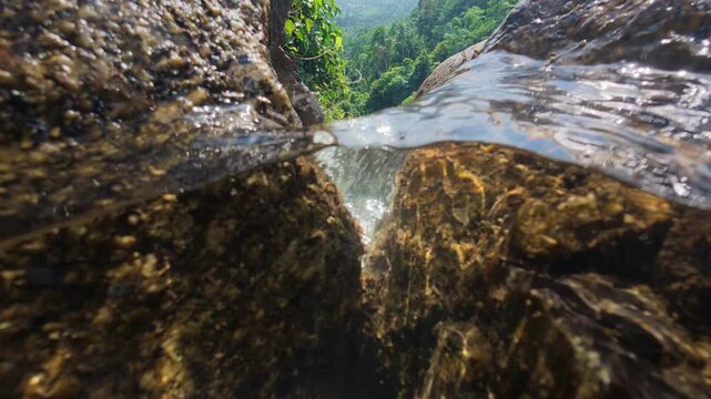 Half underwater view of crystal clear stream flowing over granite rocks at Na Muang Waterfall 2 on Koh Samui, Thailand. Split level perspective