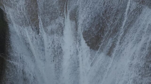 Water rushes over lip of waterfall and falls down steep rock cliff into natural pool