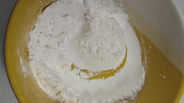 Top view panning shot of white flour ingredients inside a yellow bowl for homemade baking recipe
