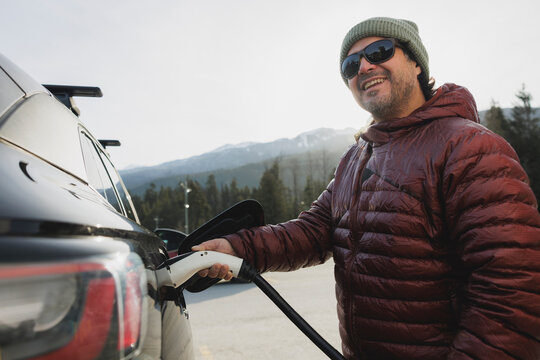 Smiling man charging his electric vehicle in mountains