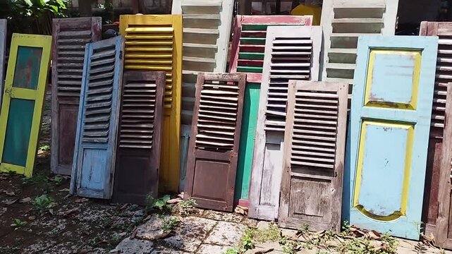 Panning shot of various colorful vintage javanese wooden shutters leaning against a wall for traditional home decoration or upcycling materials