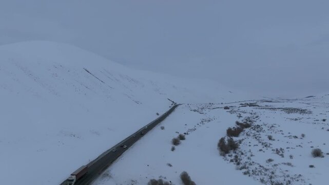 Aerial view of a highway cutting through snow-covered hills at Ala-Bel Pass, Jalal-Abad Region, Kyrgyzstan, with vehicles driving in winter weather