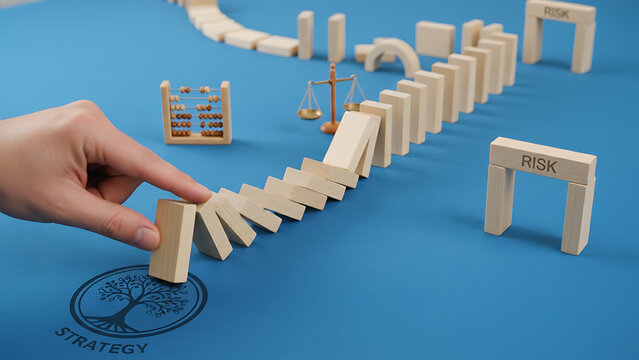 Intentional human hand poised to push wooden block triggering domino effect on blue background, representing strategic risk management, sequential chain reaction, and principle of cause and effect.