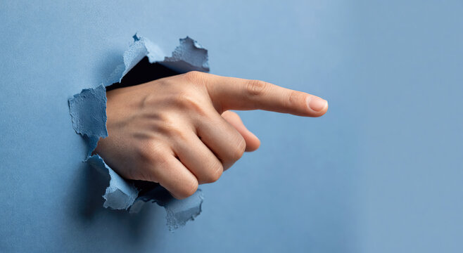 Woman hand pointing finger through a torn blue paper hole. Concept of direction, choice and discovery. Symbolic gesture of communication and information highlighted by a rip in background.