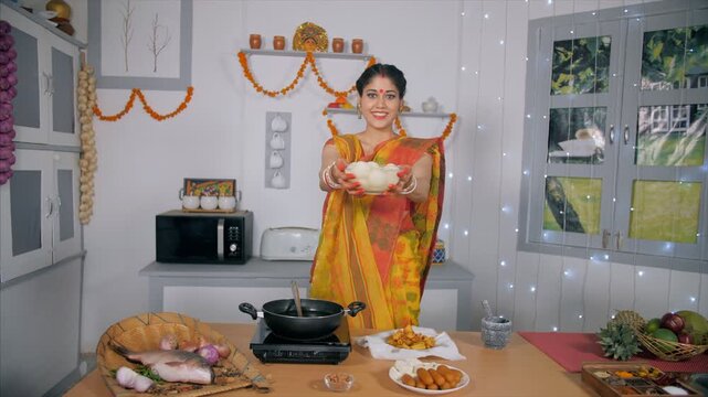 A traditional Bengali woman offering a bowl full of sweets (Rasgulla) to her guests. An Indian housewife in a Bengali saree standing in her kitchen giving Rosogolla - festival mood