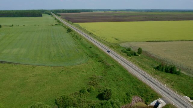 Drone footage of a straight country road cutting through green agricultural fields and meadows, with a small bridge and sparse traffic in a wide flat landscape
