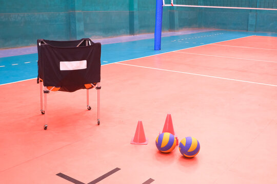 Indoor volleyball training equipment on court with ball cart, volleyballs, and cones. Concept of sports coaching, athletic practice and physical education in a gym