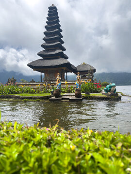 Ulun Danu Beratan Temple with multi-tiered meru tower on Lake Beratan, Bedugul, Bali, with statues, flowers, and misty mountains.