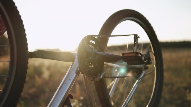 Rotation of pedals, bicycle wheel in upside down at sunset in field, medium shot. Cyclist identifying malfunction, checking operability of bicycle during ride. Movement of bicycle chain in mechanism.