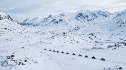 Aerial view of snow mobiles traveling across a snowy arctic tundra in the high mountains on a cold winters day.  © pinan