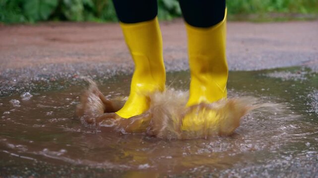 Yellow rain boots splashing in puddle on rainy day