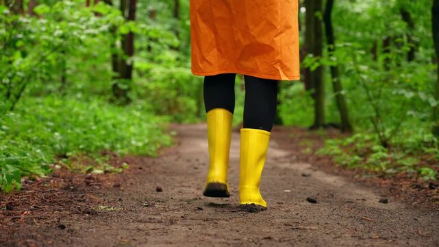 Person in raincoat and yellow boots on rainy forest path